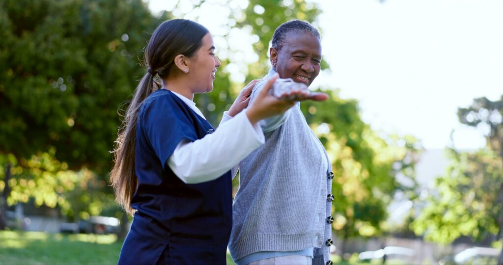 Senior, woman and caregiver with arm stretching for exercise, workout or fitness in a park with smi